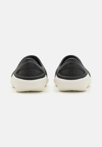 Svarta slip-on skor med en texturerad ovansida, vit texturerad sula med cirkulära detaljer. "CROCS"-logotypen präglad på hälen.