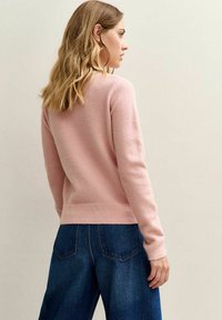 Lichtroze, gebreide trui met een ronde hals en geribde manchetten, gecombineerd met wijde blauwe denim jeans. De geweven stof is zacht.