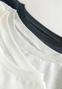 Four crewneck T-shirts in white, light gray, dark gray, and black. Ribbed necklines and soft fabric texture, neatly stacked.