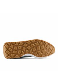 Pohja kenkien kumipinta, jossa on teksturoitu vaaleanruskea pinta, jossa on timantinmuotoisia kuvioita ja valkoinen kantapääkorostus. "New Balance" -brändäys näkyvillä.