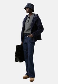 Modelka ma na sobie granatową polarową kurtkę, szary dzianinowy golf, ciemnoniebieskie szerokie dżinsy, beżowe buty na platformie oraz szary pikowany kapelusz bucket, trzymając czarną torbę z futra syntetycznego.