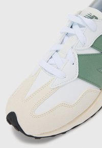 Sneaker avec une tige en cuir blanc et en daim, accents vert clair, semelle intermédiaire beige texturée et lacets blancs. Semelle extérieure en caoutchouc noir.