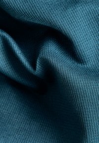 Gros plan sur un tissu en maille côtelée bleu sarcelle foncé avec des plis doux et des ombres mettant en valeur le motif texturé.