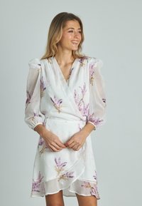 Weißes Wickelkleid mit lila floralem Muster, Puffärmeln und gewelltem Saum. Hergestellt aus leichtem Stoff mit einer weichen, fließenden Textur.