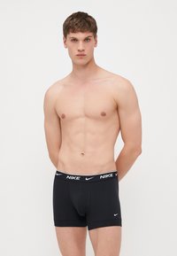 Fekete pamut bokszergyümölcs nadrág elasztikus derékpánttal, amelyen fehér Nike logó található. Fitt fazon és sima szövettextúra.