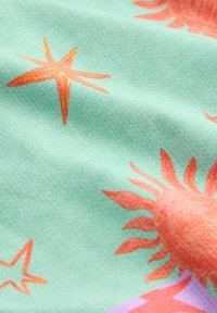 Világoskék anyag narancssárga nap- és tengeri csillag mintákkal, amely bemutatja a textúrát és az enyhe redőket.