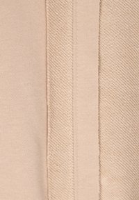 Tessuto beige con una trama testurizzata, finitura liscia e dettagli di cucitura visibili. Due sezioni di tessuto contrastante sono unite insieme.