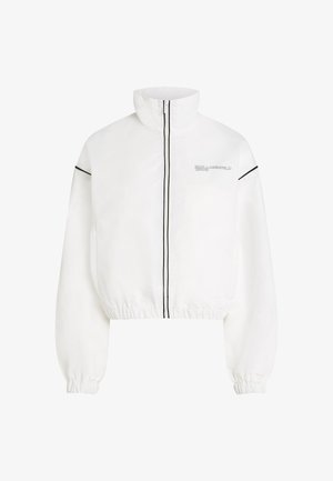 Balta trumpa striukė su aukštu apykakle, priekiniais užtrauktukais, juodomis kontrastingomis juostelėmis ir elastingomis rankovėmis, su logotipo detale ant krūtinės.