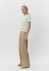 Rövid ujjú, világoskrém színű póló, amelyet magas derekú, bőszárú bézs nadrággal párosítanak. Simább anyag finom varrással és laza szabással.