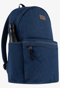 Blå denimryggsäck med rund topp, brun läderlogotyp, framficka och sidficka för en vattenflaska i rostfritt stål.