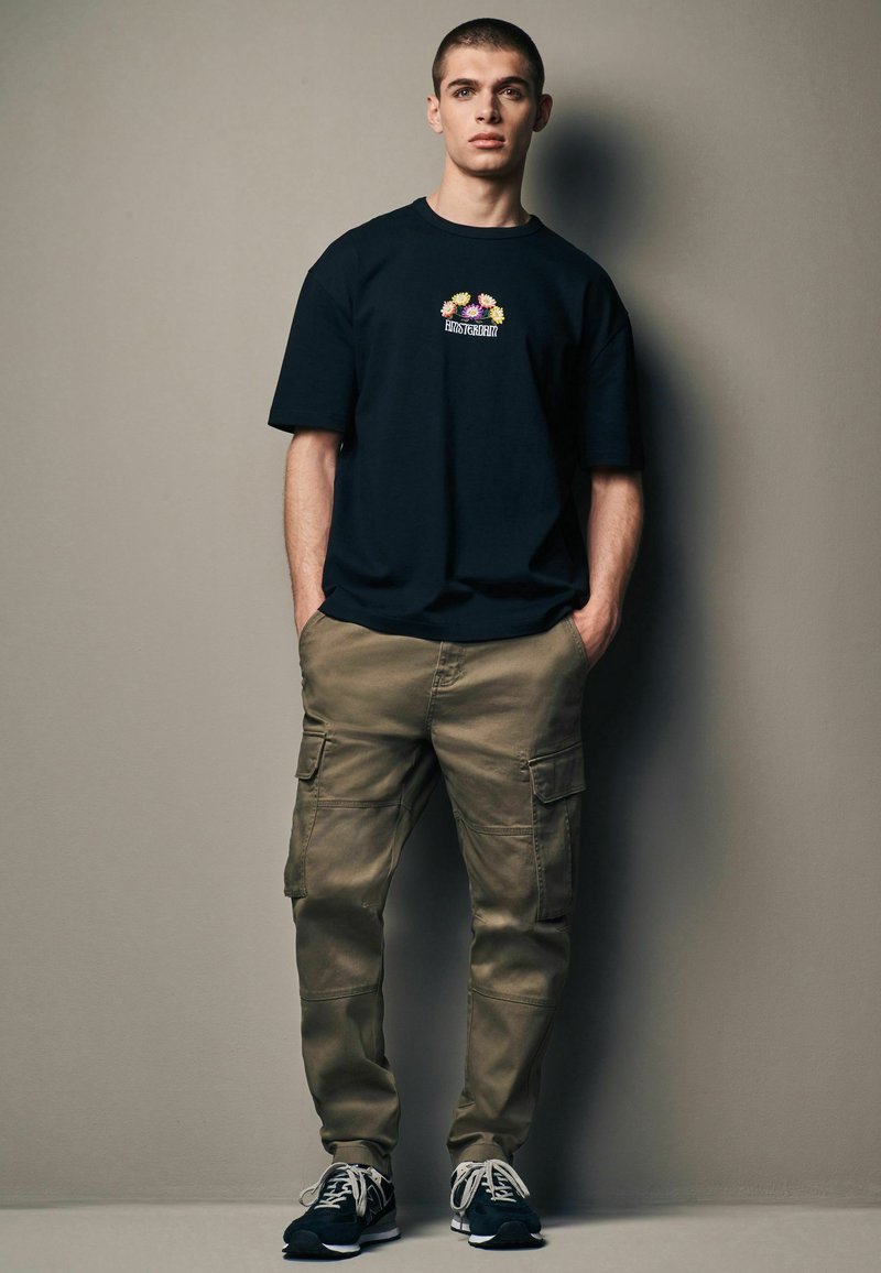 Czarny bawełniany t-shirt z krótkim rękawem i graficznym nadrukiem kwiatowym z przodu, w połączeniu z beżowymi spodniami cargo z wieloma kieszeniami i luźnym krojem.
