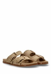 Las sandalias de ante en color marrón presentan dos correas anchas con detalles en hardware dorado y remaches. Suela plana y diseño abierto para un uso fácil.