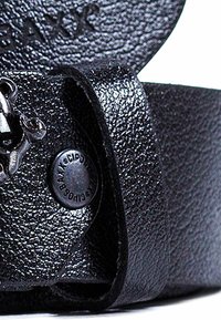 Zwarte leren band met een gestructureerd oppervlak, stevige metalen hardware en een cirkelvormig logo-detail. Het ontwerp is stijlvol en minimalistisch.