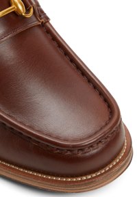 Mocassin en cuir marron avec bout arrondi, surpiqûres contrastantes et garniture dorée. Texture lisse avec une finition élégante.