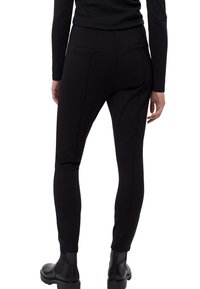 Pantalon noir ajusté avec poches arrière, tissu lisse, coupe fuselée et taille mi-haute, associé à des bottines noires.