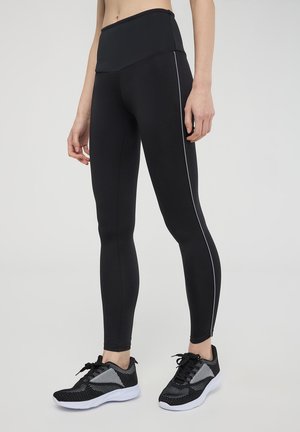 Leggings neri con una vita alta, caratterizzati da un design elegante e una striscia laterale bianca a contrasto. Abbinati a sneakers nere in rete.