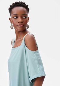 Jasnoniebieski top bez ramiączek z luźnymi rękawami i misternymi detalami na ramiączkach. Gładki materiał o swobodnym kroju i prostym wzorze.