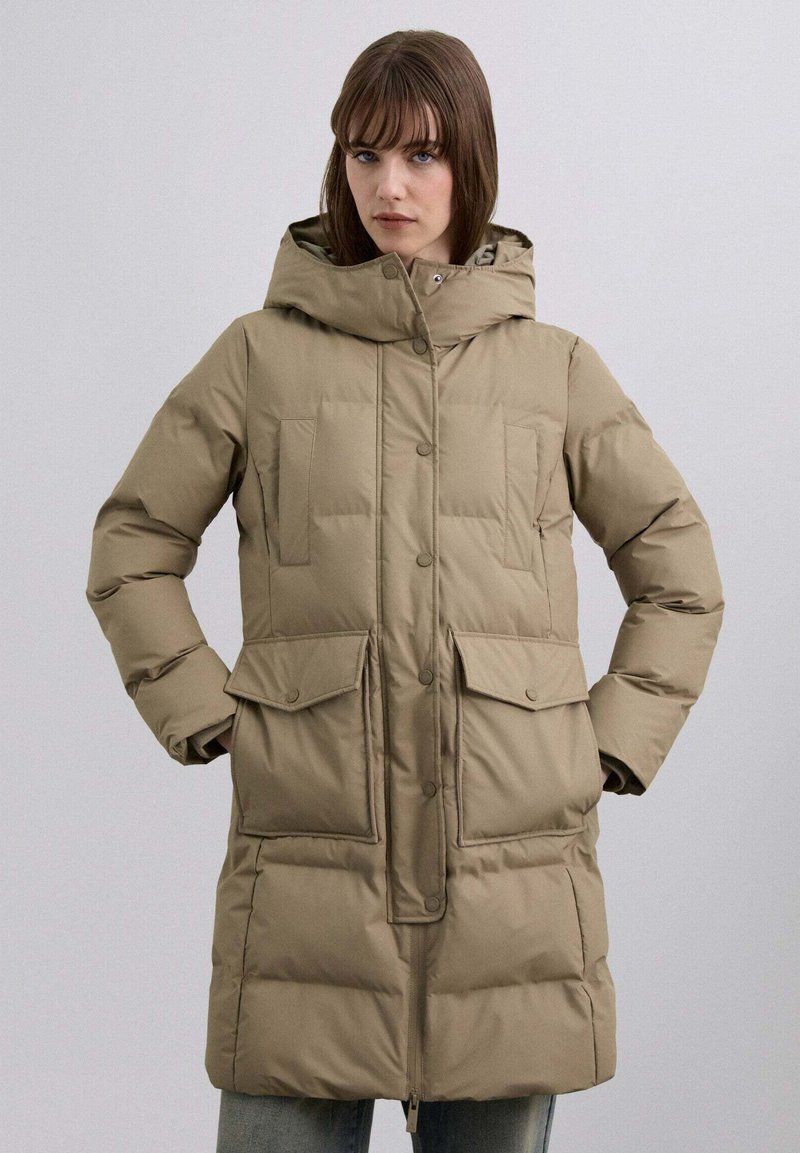 Abrigo acolchado beige con capucha, que cuenta con cierre de cremallera y botones, dos grandes bolsillos delanteros y un diseño acolchado.