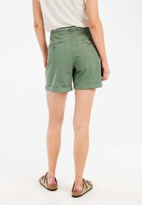 Groene katoen shorts met opgerolde zoom, twee achterzakken en knoopdetails. De stof heeft een gladde textuur met een lichte glans.
