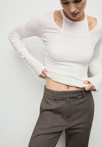 Top a maniche lunghe bianco a costine con un design aderente, abbinato a pantaloni grigi su misura con una superficie liscia e passanti per la cintura.