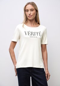 Creamfarvet, blødt bomulds t-shirt med korte ærmer, en rund halsudskæring og sort trykt tekst: "VÉRITÉ club de la rue."
