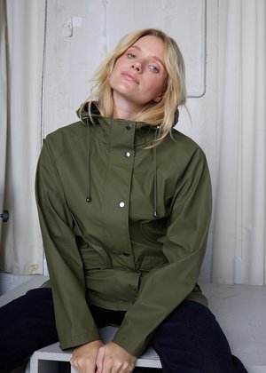 Ūdensizturīga olīvu zaļa jaka ar kapuci, kas sašaurināms ar auklu, sprādzēm un jostas siksnu. Gluda, matēta virsma ar sānu kabatām.