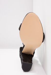 Sandale compensée noire texturée avec une semelle beige lisse, vue par le dessous sur fond blanc.