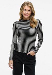 Randig långärmad topp i grått och svart ribbat tyg, med en vågig u-ringning och nederkant, stylad med svarta byxor.