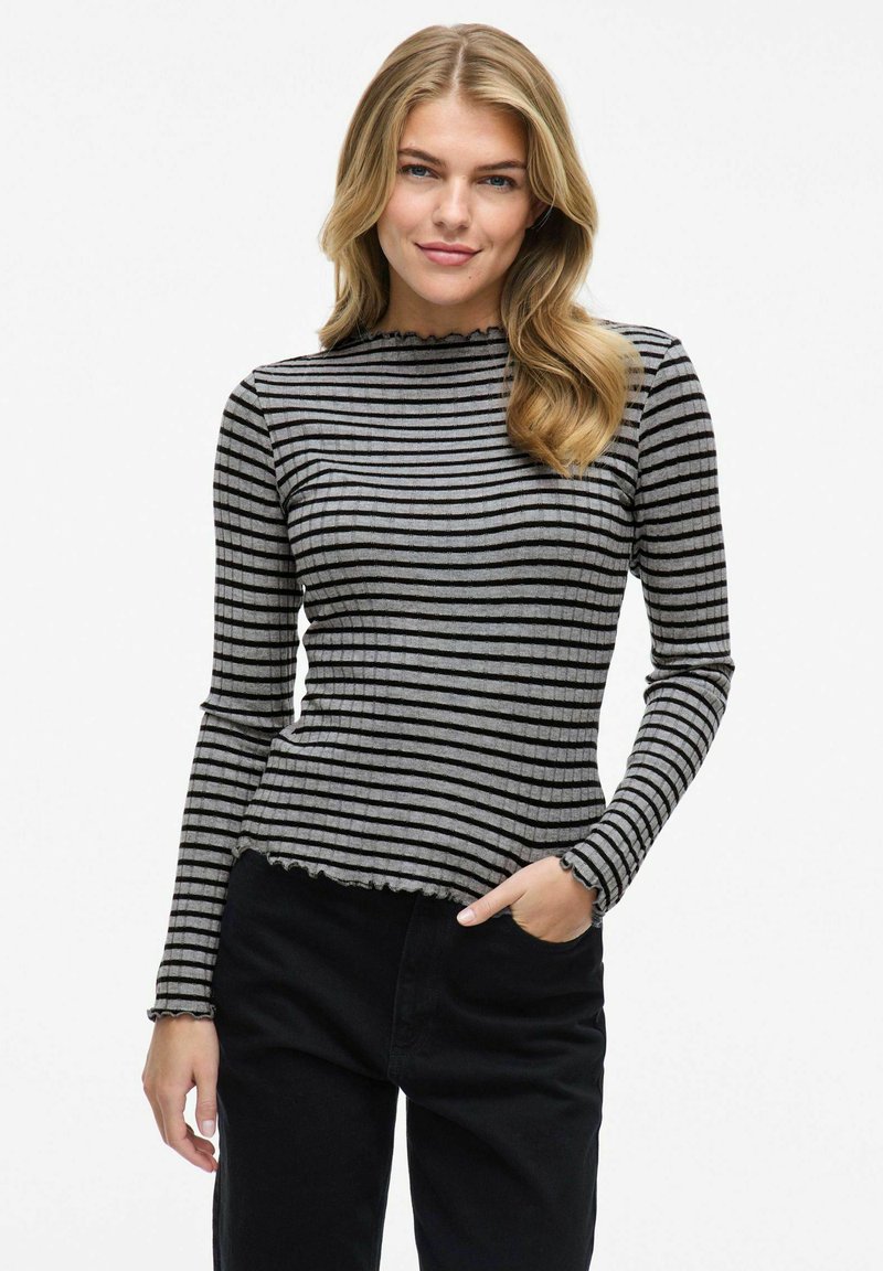 Randig långärmad topp i grått och svart ribbat tyg, med en vågig u-ringning och nederkant, stylad med svarta byxor.