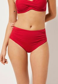 Röd bikiniuppsättning med ett inlindat topp i mjukt tyg och högmidjade byxor som har rynkningar på sidorna för en strukturerad look.