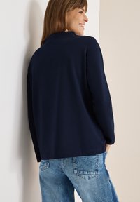 Top de manga larga azul marino hecho de una tela suave, con cuello y un corte relajado, combinado con jeans de mezclilla azul claro.