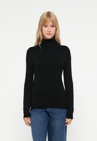 Suéter preto de gola alta feito de um tecido de malha suave, com mangas longas e silhueta ajustada, combinado com jeans de ganga azuis.