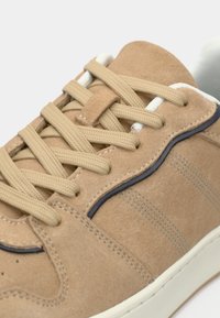 Καφέ σουέτ αθλητικά παπούτσια με μπεζ κορδόνια, ναυτικές λεπτομέρειες και λευκή ενδιάμεση σόλα. Διαθέτει διακριτικές ραφές και υφασμάτινα πλαϊνά πάνελ.