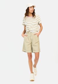 Gestreifes Baumwoll-T-Shirt mit beigen und weißen Streifen und knotetet Vorderseite. Helle beige Shorts mit Taschen und Umschlägen, kombiniert mit weißen Sneakern.
