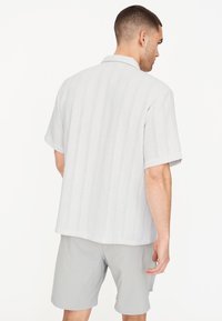 Camisa de manga corta texturizada en gris claro con rayas verticales y cuello, combinada con pantalones cortos gris claro.