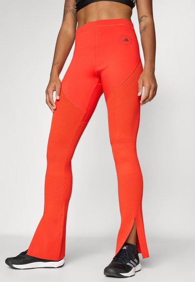 Leggings de sport rouge avec texture côtelée, design évasé, fentes latérales et un logo à la hanche. Fabriqués à partir d'un matériau extensible et respirant.