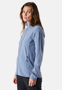 Giacca in fleece azzurro chiaro con collare alto, zip frontale e tasche laterali con zip. Presenta maniche lunghe e una texture morbida.