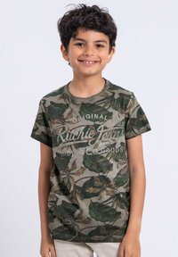 T-shirt vert camo avec un motif de feuilles et un imprimé en texte blanc. Manches courtes et col rond. Tissu doux avec une coupe décontractée.