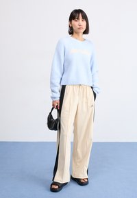 Light blue fuzzy sweater with "Jordan" text, paired with beige wide-leg pants featuring black side stripes and black slip-on platform sandals.