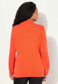 Orange tröja med hög krage, långa ärmar och ribbad nederkant. Mjuk textur med en figurnära silhuett, sedd från baksidan.