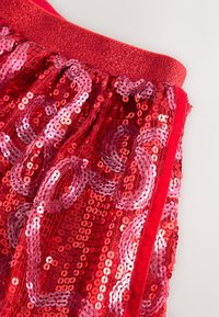 Tessuto rosso con paillettes lucide, caratterizzato da paillettes circolari e un motivo decorativo a onde. Vita elastica rossa che borda la parte superiore.