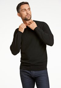 Czarny sweter z długim rękawem wykonany z dzianiny, z okrągłym dekoltem i ściągaczami na rękawach. Połączony z ciemnoniebieskimi dżinsami.