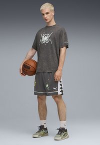 Grå grafisk t-shirt med trykt design, parret med grå shorts med farverige splatterdetaljer og sorte zigzag-detaljer. Basketball i hånden.
