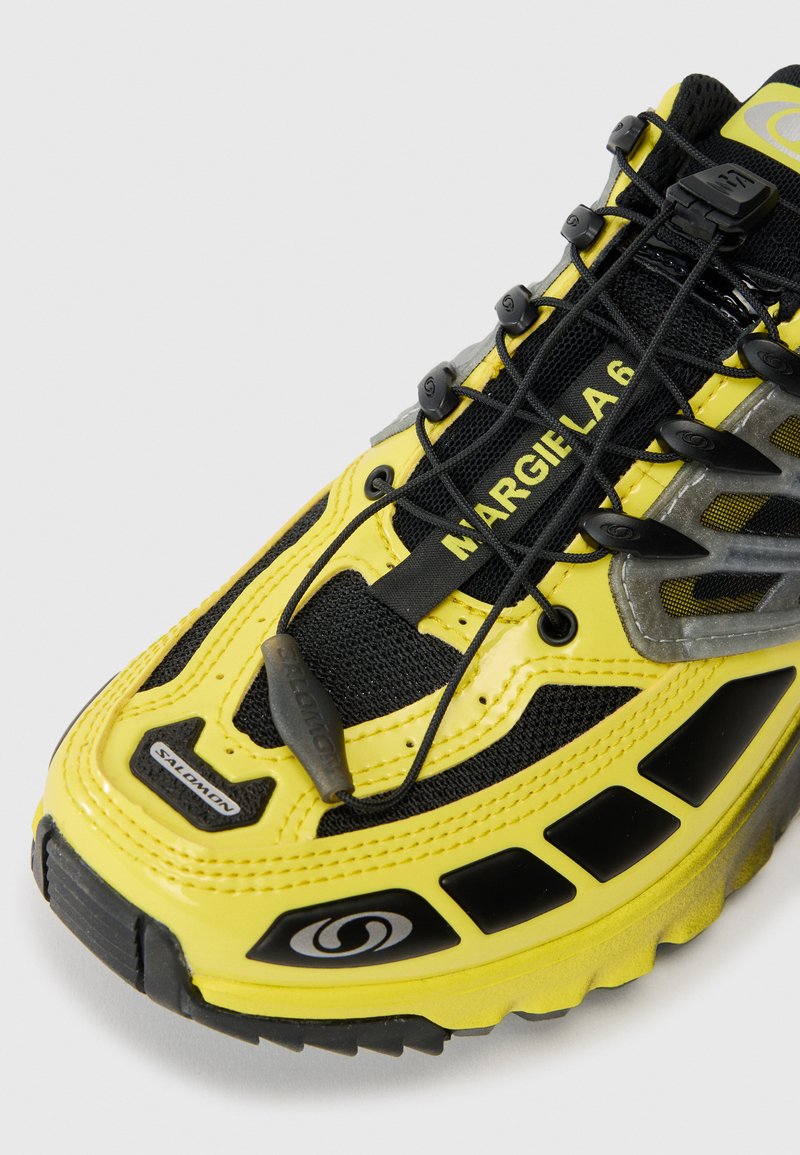 Gul- og sort Salomon-sneaker med elastisk hurtigløbesystem og "MARGIELA 6" tekst på tungen.