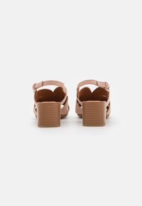 Paire de sandales à talons blocs en daim beige avec brides à la cheville et fermetures à boucle argentée, vues de dos sur fond blanc.
