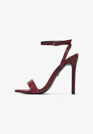 Sandalia de tacón alto con estampado de piel de serpiente roja, con dos correas delgadas: una sobre los dedos y otra con hebilla alrededor del tobillo, exhibida sobre fondo blanco.