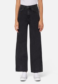 Široké černé džíny vyrobené z denimu, s vysokým pasem a viditelným švy. Kombinované s bílými teniskami pro kontrast.