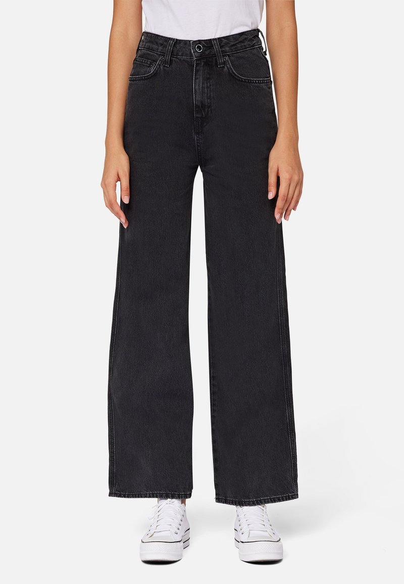 Široké černé džíny vyrobené z denimu, s vysokým pasem a viditelným švy. Kombinované s bílými teniskami pro kontrast.