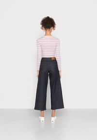 Calças de ganga de perna larga em denim escuro com uma cintura alta e um remendo de couro castanho na parte de trás, combinadas com uma blusa de manga longa às riscas em cores pastel.