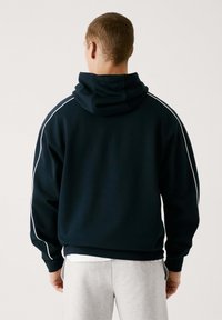 Sudadera con capucha color marino con rayas laterales blancas, que cuenta con un bolsillo tipo canguro y puños acanalados. Tejido suave, corte relajado, diseño minimalista.